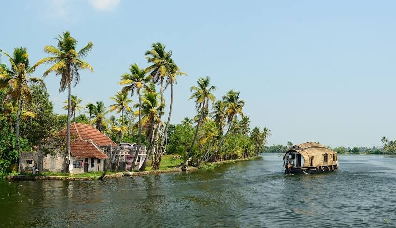 Scenic view of Kerala, God’s Own Country, with serene backwaters, lush coconut palms, and traditional houseboats gliding on calm waters.